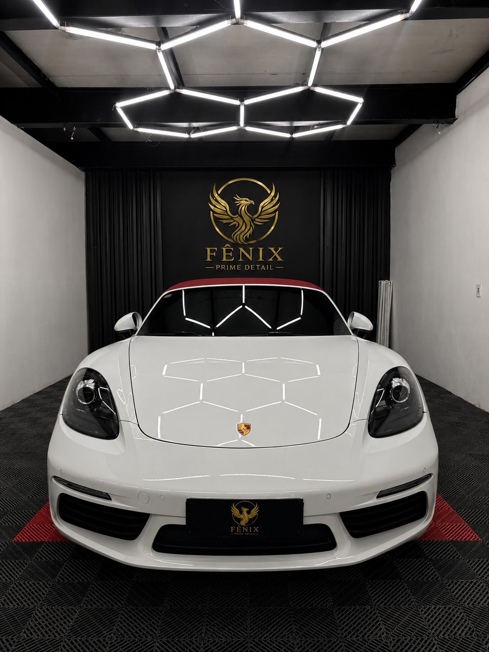 Porsche 718 branco de frente no estúdio da Fênix Prime Detail com a logo dourada ao fundo