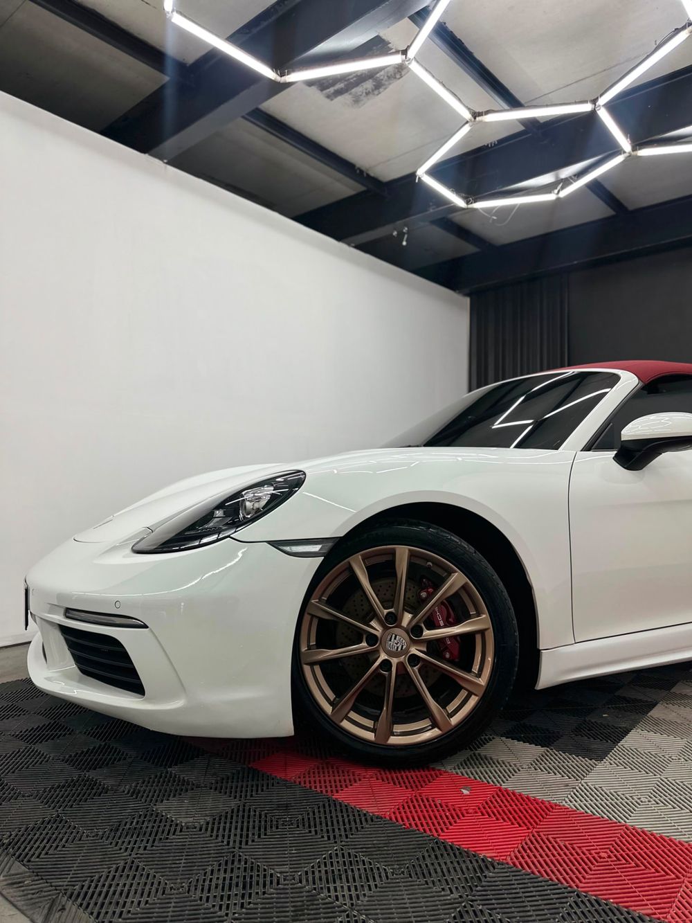 Lateral do Porsche 718 branco com rodas douradas após lavagem técnica detalhada